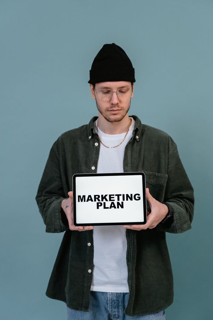 gallery-2 Adult wearing casual clothing holding a tablet that reads 'Marketing Plan'.